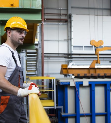 Portrait of male factory worker leaning on metal railings in industrial production hall.
